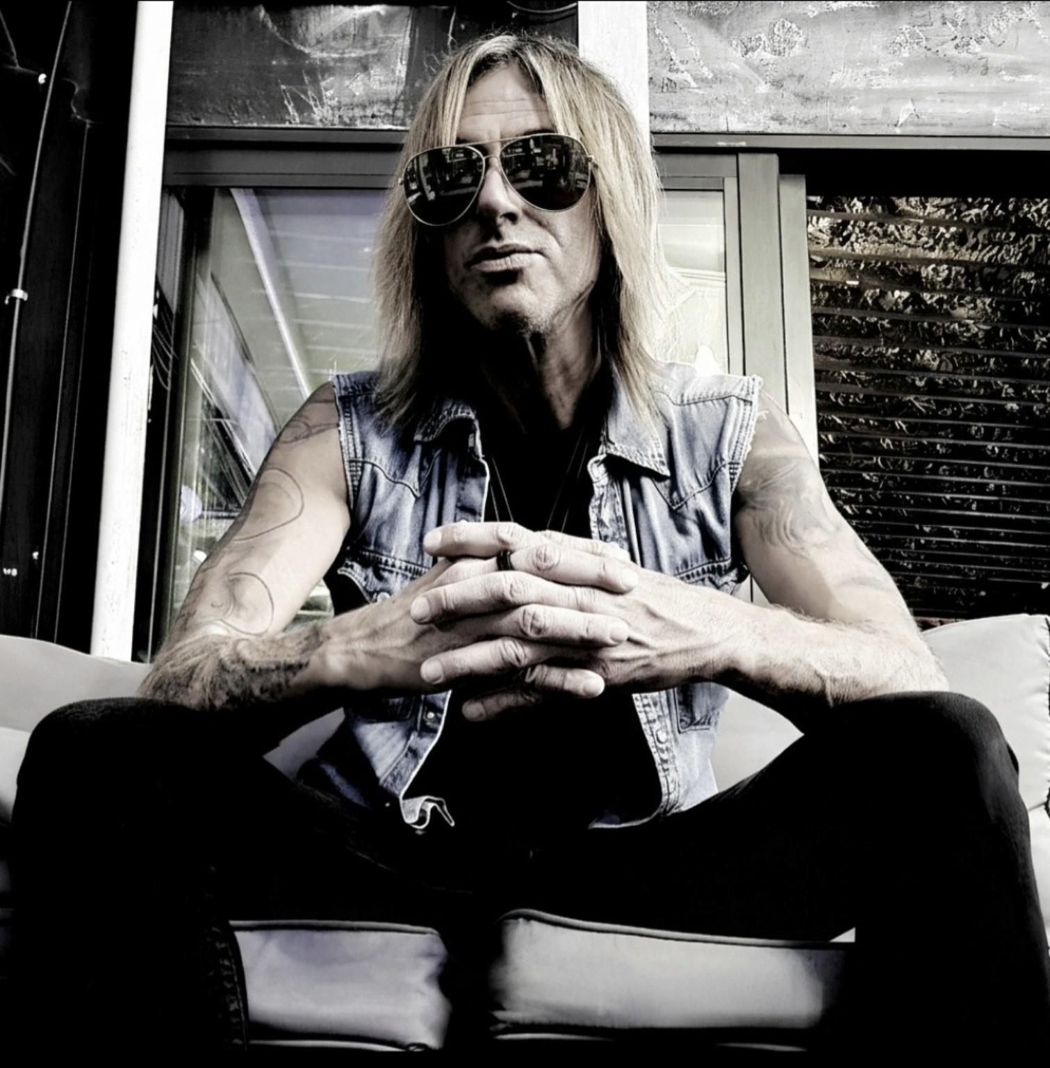 Anthony Picone seated with hands clasped, wearing aviator sunglasses and a sleeveless denim vest